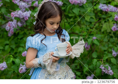 Caucasian child in blue dress enjoying tea in garden with lilac flowers Caucasian child in blue dress enjoying tea in garden with lilac flowers 123679756