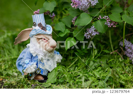 Decorative white rabbit figurine in blue victorian outfit amidst lilac flowers Decorative white rabbit figurine in blue victorian outfit amidst lilac flowers 123679764