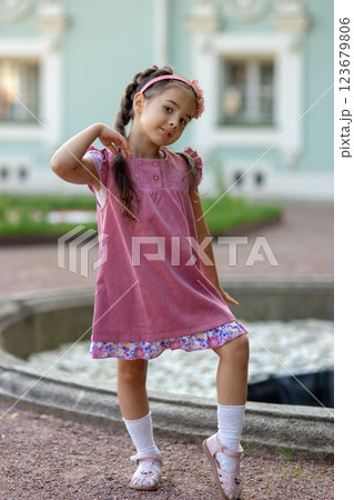 Young caucasian girl posing playfully in a pink dress near a fountain Young caucasian girl posing playfully in a pink dress near a fountain 123679806