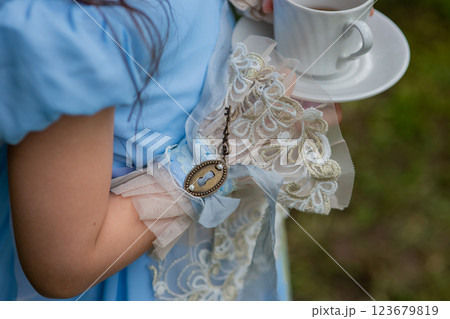 Young girl in blue victorian dress holding teacup in garden setting Young girl in blue victorian dress holding teacup in garden setting 123679819