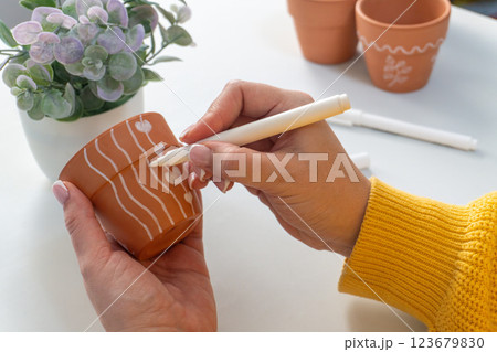 Hands decorate a terracotta pot with white marker, lines and hearts 123679830