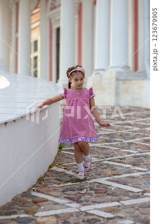 Young caucasian girl in pink dress walking on cobblestone path near classical building Young caucasian girl in pink dress walking on cobblestone path near classical building 123679905