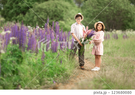 Young caucasian boy and girl in field with purple lupine flowers, smiling and holding bouquets Young caucasian boy and girl in field with purple lupine flowers, smiling and holding bouquets 123680080
