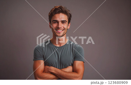 Young man with a smile on his face is wearing a gray shirt and is crossing his arms 123680909
