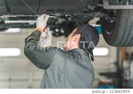 リフトで上がった車の下回りで作業・点検・整備するメカニック・整備士の男性 リフトで上がった車の下回りで作業・点検・整備するメカニック・整備士の男性 123681954