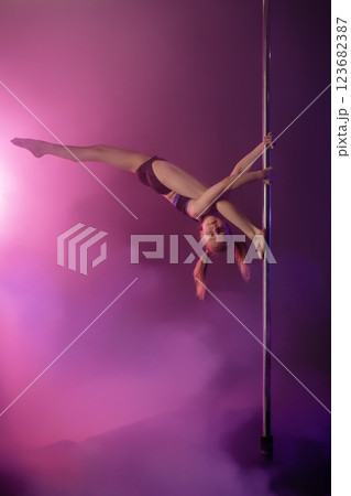 Girl performing an impressive pose on a pole with vibrant lighting effects 123682387