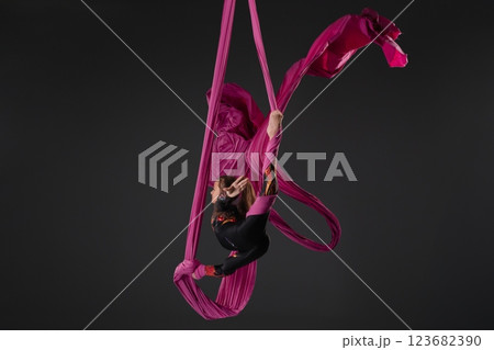 Girl performs aerial silk stunt with pink fabric in studio setting Girl performs aerial silk stunt with pink fabric in studio setting 123682390