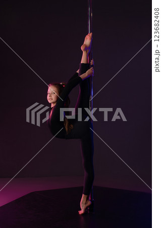 Girl performs impressive pole dance move in a studio setting at night 123682408