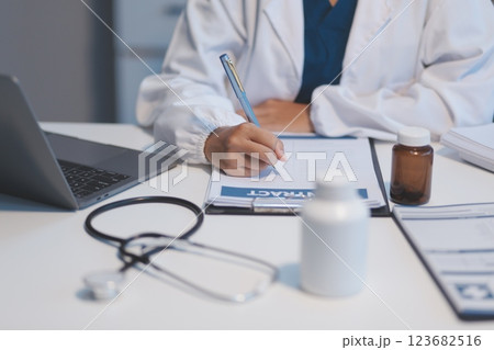 A professional and focused Asian female doctor in scrubs is working and reading medical research on her laptop in her office at a hospital. A professional and focused Asian female doctor in scrubs is working and reading medical research on her laptop in her office at a hospital. 123682516
