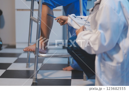 Asian young professional successful friendly female nurse in blue hospital uniform helping supporting physical therapy senior old pensioner unhealthy injury woman patient walking via four legs walker. 123682555