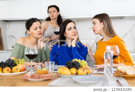 Sad Caucasian woman sits silently in kitchen, female friends sympathize and comfort woman 123683280