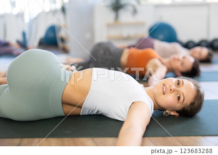 Sporty young woman doing yoga with group in studio, performing hamstring and low back stretching Ardha Pawanmuktasana Sporty young woman doing yoga with group in studio, performing hamstring and low back stretching Ardha Pawanmuktasana 123683288