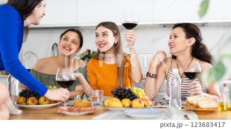Happy women congregated around a festive table; participating in animated discussions and enjoying the delights of wine Happy women congregated around a festive table; participating in animated discussions and enjoying the delights of wine 123683417