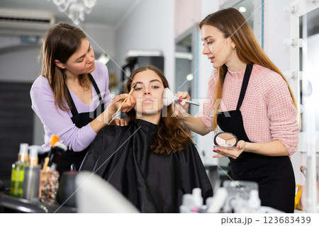 Two makeup artists apply makeup on the face of a young woman Two makeup artists apply makeup on the face of a young woman 123683439
