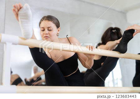 Young female ballet dancer stretching leg at barre 123683443