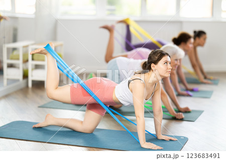 Women on hands and knees doing stretch exercises for legs with resistance band on mats in gym 123683491