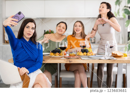 Spanish smiling girl is sitting on chair and taking selfies during gatherings with friends 123683681
