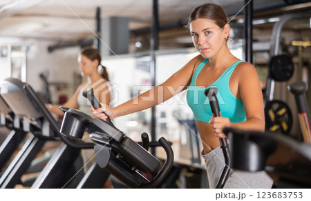 Slender athletic girl during cardio exercises on elliptical simulator in fitness center. Slender athletic girl during cardio exercises on elliptical simulator in fitness center. 123683753