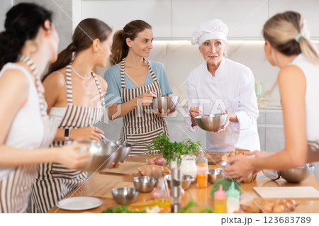Elderly woman chef with bowl in hands tells women at culinary courses about traditions of cuisine 123683789