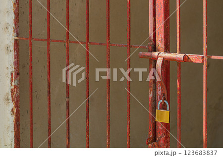 Red lattice metal gates welded from a pipe-rolling profile pipe of square cross-section, on which a closing gate with a padlock is mounted. The concept of a closed path, a road. Abstraction symbol Red lattice metal gates welded from a pipe-rolling profile pipe of square cross-section, on which a closing gate with a padlock is mounted. The concept of a closed path, a road. Abstraction symbol 123683837