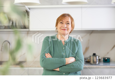 Cheerful senior woman standing in her kitchen smiling Cheerful senior woman standing in her kitchen smiling 123683977