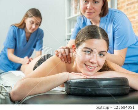 Smiling girl getting relaxing massage from two masseuse Smiling girl getting relaxing massage from two masseuse 123684051