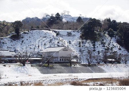 冬の晴れ間の明るい空に映える雪化粧した月山富田城跡と麓の道の駅の風景：島根県 安来市 広瀬町 123685004