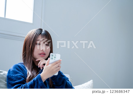 冬のリビングでスマホを見て悩む女性 123686347