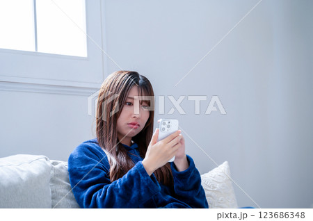冬のリビングでスマホを見て悩む女性 123686348