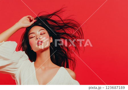 Confident woman with flowing hair poses against vibrant red background in expressive fashion statement Confident woman with flowing hair poses against vibrant red background in expressive fashion statement 123687189