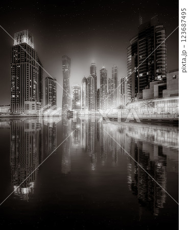 Urban city skyline with illuminated skyscrapers and waterfront railing in black and white at night, Dubai Marina bay UAE 123687495
