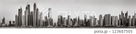 Monochrome city skyline with tall skyscrapers reflecting on calm water under a cloudy sky, Dubai Marina bay UAE 123687505