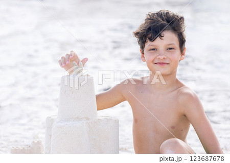 Teen boy is constructing a sand castle at the seashore beach. 123687678