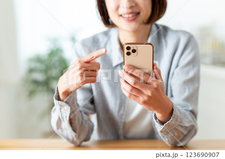 家のリビングで笑顔でスマホを指差すミドル女性 123690907