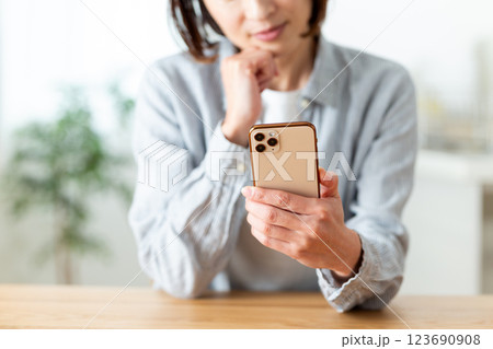 家のリビングでスマホを持って悩むミドル女性 123690908