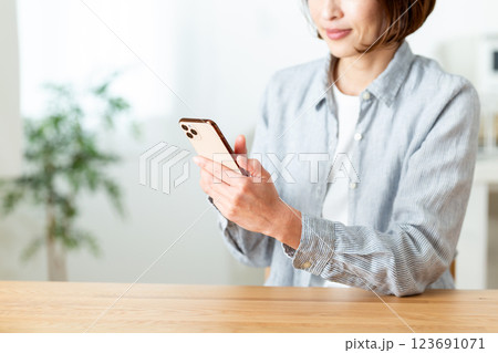 家のリビングでスマホを見て微笑むミドル女性 家のリビングでスマホを見て微笑むミドル女性 123691071