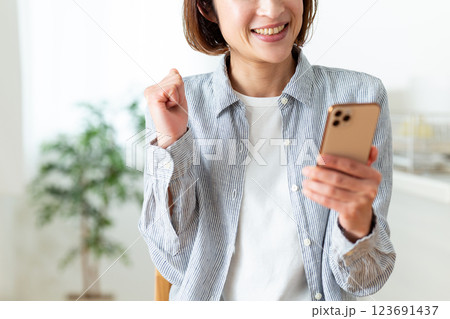 家のリビングでスマホを見て喜ぶミドル女性 123691437