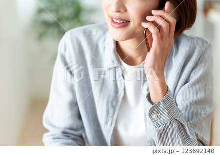 家のリビングで笑顔でスマホ通話するミドル女性 123692140