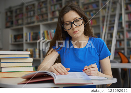 Smart woman in eyeglasses feeling dreamy while spending time in library 123692932