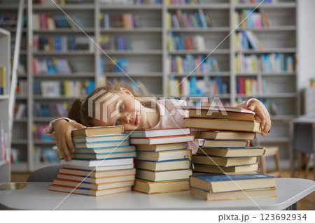 Happy glad little school girl child hugging stack of textbooks in library 123692934