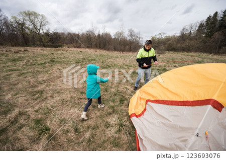 Creating family memories while camping in the great outdoors with a child pitching a tent on a cloudy afternoon in a serene nature setting Creating family memories while camping in the great outdoors with a child pitching a tent on a cloudy afternoon in a serene nature setting 123693076
