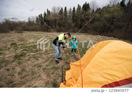 Setting up a colorful tent while enjoying quality time outdoors during a chilly day in early spring near a peaceful, wooded area Setting up a colorful tent while enjoying quality time outdoors during a chilly day in early spring near a peaceful, wooded area 123693077