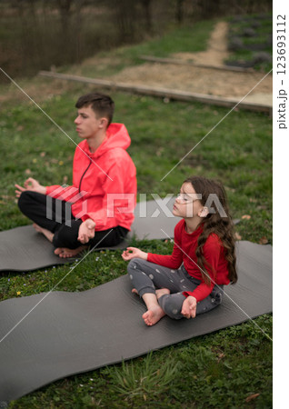 Mindful moments in nature as a boy and girl practice yoga on mats, embracing tranquility during a serene afternoon under the soft glow of sunlight 123693112