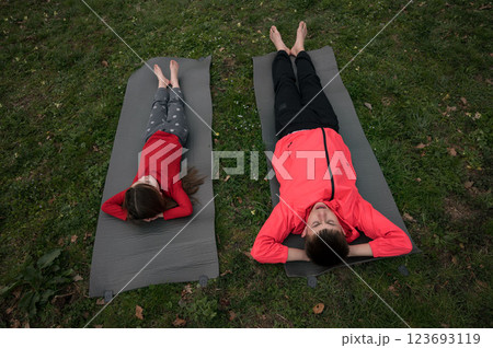 Relaxing in the sun, two children enjoy a sunny afternoon outdoors on yoga mats in a grassy park, soaking up warmth and tranquility surrounded by nature 123693119