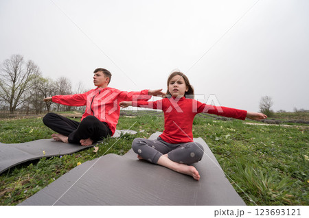 Young practitioners engage in yoga poses in a serene field on a cloudy day, embracing nature and tranquility while enhancing their focus and mindfulness 123693121