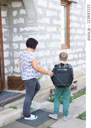 A woman sees her grandson off to school, gently placing a hand on his back as he prepares to leave, showing love and support. 123693123