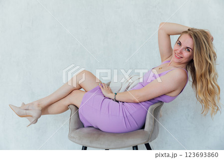 Beautiful blonde woman sitting on a chair in purple summer dress 123693860
