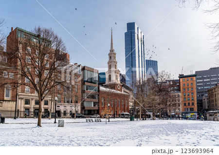 View of Park Street Church and surrounded buildings in Boston during winter with snow on the Boston Common ground and flock of birds flying against clear blue sky View of Park Street Church and surrounded buildings in Boston during winter with snow on the Boston Common ground and flock of birds flying against clear blue sky 123693964