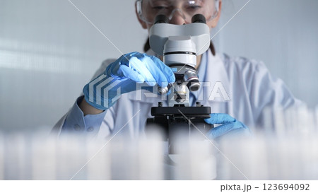 Woman scientist wearing lab coat, white protective gloves and glasses, is using microscope in modern laboratory setup, portrait view. Low key lighting photo. Science and Medicine Woman scientist wearing lab coat, white protective gloves and glasses, is using microscope in modern laboratory setup, portrait view. Low key lighting photo. Science and Medicine 123694092