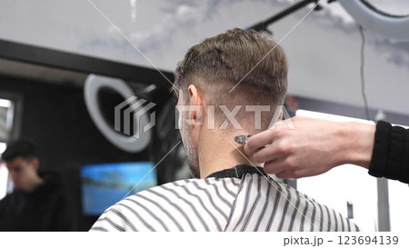 Skilled barber trimming client's neck hairline, wielding straight razor with expertise in traditional, vintage style barbershop setting Skilled barber trimming client's neck hairline, wielding straight razor with expertise in traditional, vintage style barbershop setting 123694139